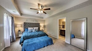 A bedroom with a tufted headboard, a bed with blue bedding, a ceiling fan, and a large mirror. - Percy priest Lake House (La Vergne)