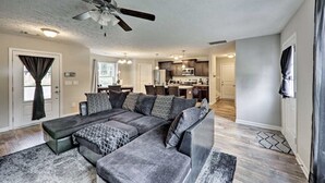 A modern living room with a sectional sofa, a ceiling fan, and a kitchen in the background. - Percy priest Lake House (La Vergne)
