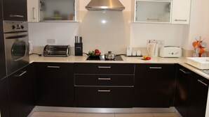 A modern kitchen with dark cabinets, a stainless steel range hood, a toaster, a kettle, and a sink.
