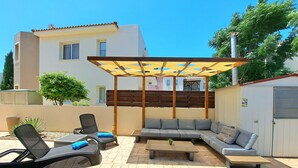 A patio area with a wooden pergola, a grey sofa, and two lounge chairs.