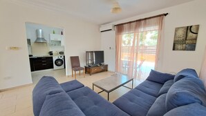 A living room with a large blue sofa, a TV, and a dining area with a table and chairs.