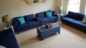 Un salon avec deux canapés bleus, un pouf assorti et un tableau représentant une scène de plage, accroché au mur.