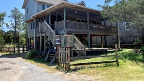 A two-story wooden house with a balcony, a porch, and a fenced driveway.
