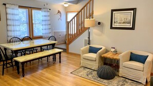 A dining area with a wooden table and chairs, a bench, a staircase, and a small side table with a lamp.