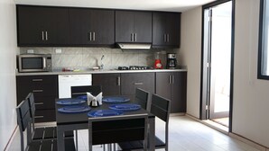 Eine moderne Küche mit dunklen Schränken, einer Mikrowelle, einer Kaffeemaschine und einem Esstisch mit blauen Platzdeckchen.