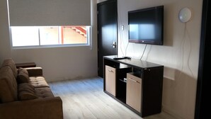 Ein modernes Wohnzimmer mit einer Couch, einem an der Wand befestigten Fernseher und einem Schreibtisch mit einem Computer.