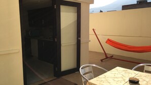 Ein Balkon mit Tisch, Stühlen, einer Hängematte und einer Schiebetür zum Küchenbereich.