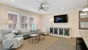 A spacious living room with a sofa, armchairs, a coffee table, and a TV mounted on the wall. - Stunning updated cottage on the beach! (Orange Beach)
