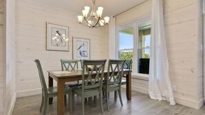 A dining area with a wooden table and chairs, framed artwork on the wall, and a chandelier. - Stunning updated cottage on the beach! (Orange Beach)