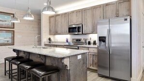 A modern kitchen with wooden cabinets, stainless steel appliances, and a central island with bar stools. - Stunning updated cottage on the beach! (Orange Beach)