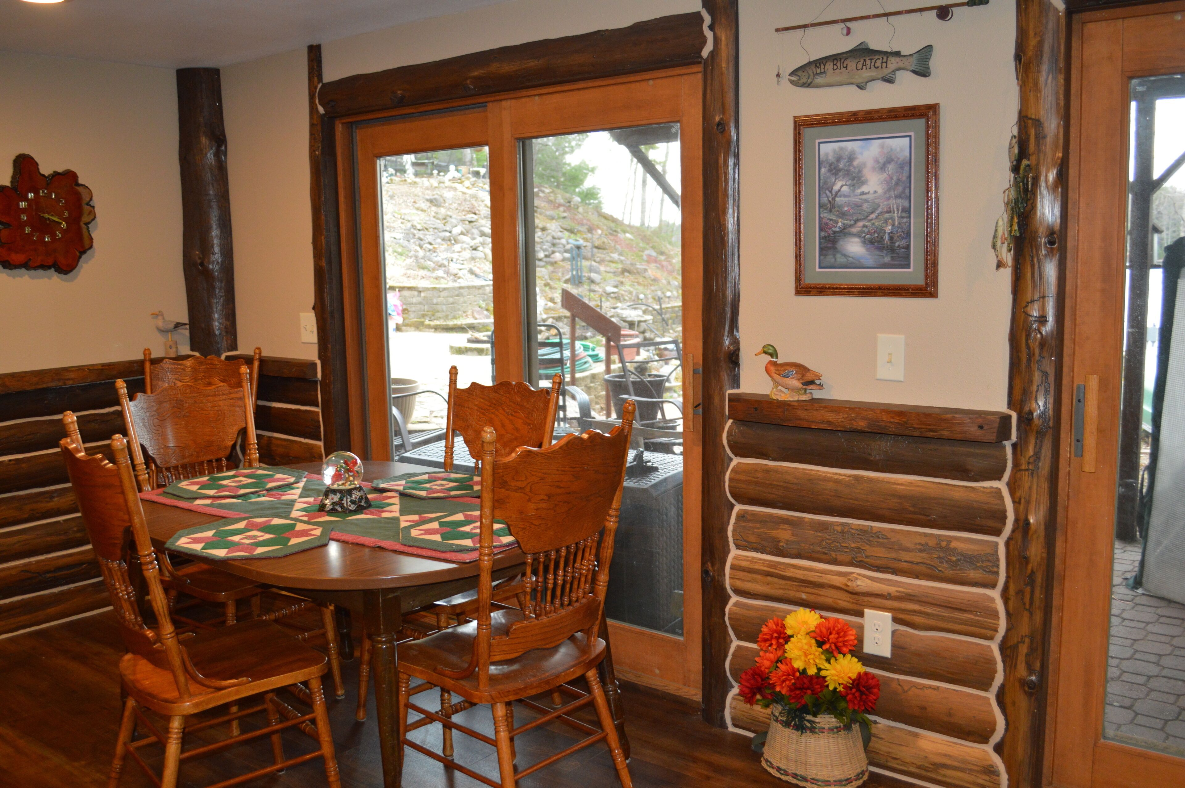 Une table de salle à manger en bois avec des chaises, une porte vitrée donnant sur l’extérieur, un banc en bois et une décoration murale représentant des poissons.