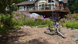 A two-story house with a balcony, a deck, and a garden with various plants and flowers.