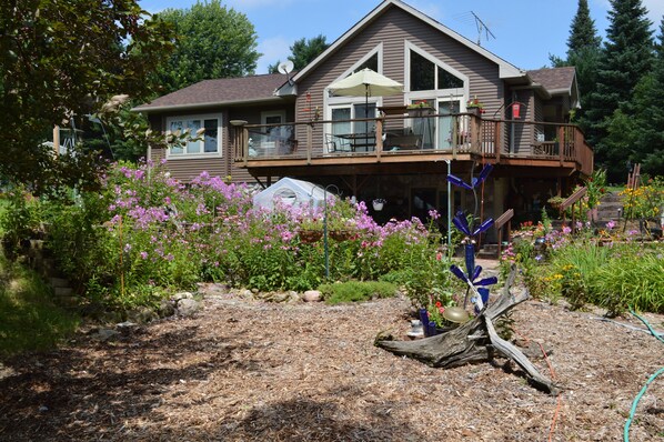 A two-story house with a balcony, surrounded by a garden with various plants and flowers.