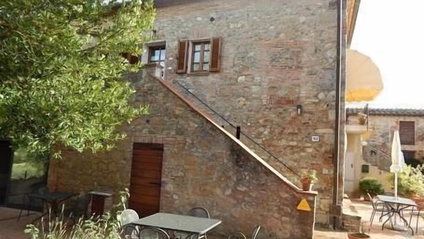 Un edificio de piedra con una escalera que lleva a una puerta de madera, asientos exteriores y plantas en macetas.