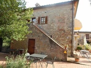 A stone building with a staircase leading to a wooden door, outdoor seating, and potted plants. - 2 rooms apartment for 4 people in the countryside close to Siena (SIENA)