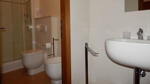 Un baño con ducha, dos inodoros, un lavabo y un espejo.