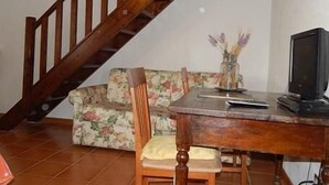 Una escalera de madera, un sofá floral, una mesa de comedor de madera con un televisor y un jarrón con flores.