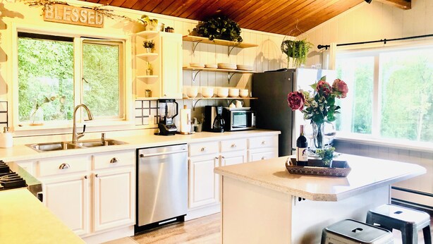 A kitchen with white cabinets, a stainless steel dishwasher, a black refrigerator, and a wooden ceiling. - Lovely 3br/2ba Hideaway! Great for Groups & Families! Inlet & Denali Views (Anchorage)