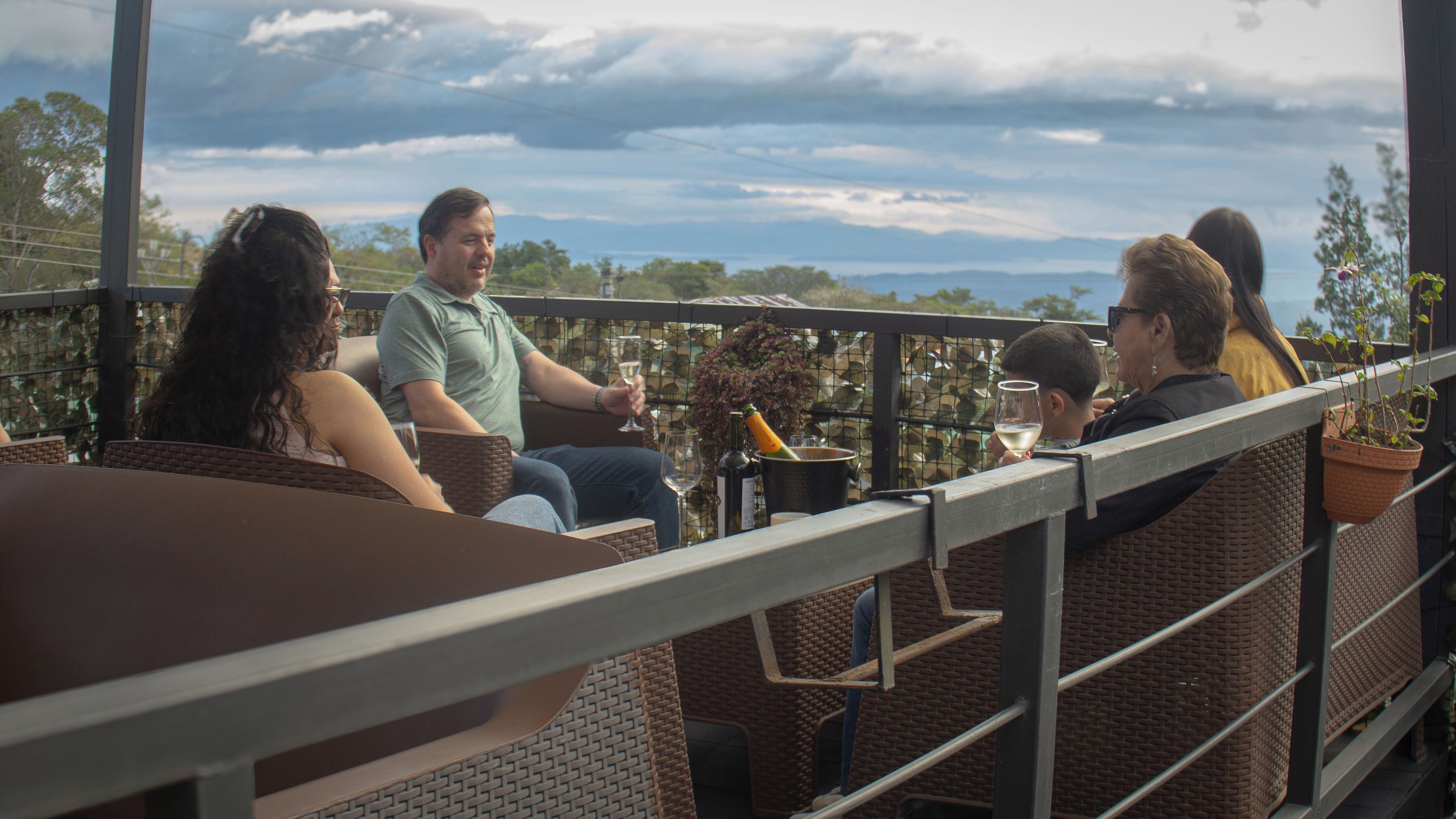 A group of people seated at a table with a view of the sky and distant landscape.