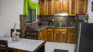 A kitchen with wooden cabinets, a granite countertop, a dining table with chairs, and a refrigerator.