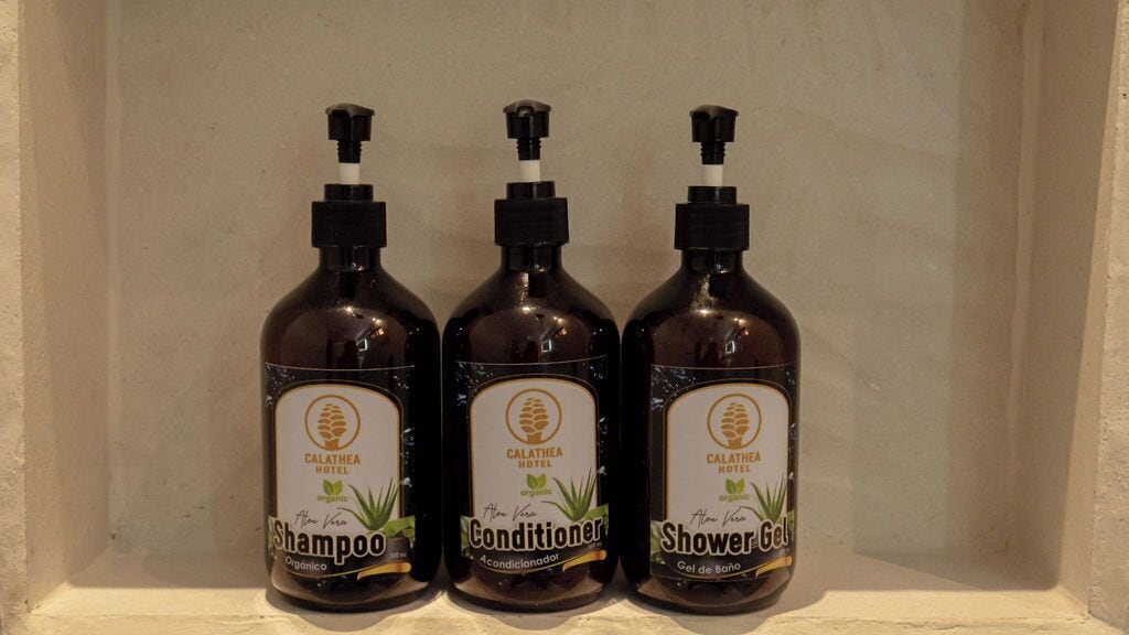 Three bottles of Calathea Hotel organic shampoo, conditioner, and shower gel in a shelf.