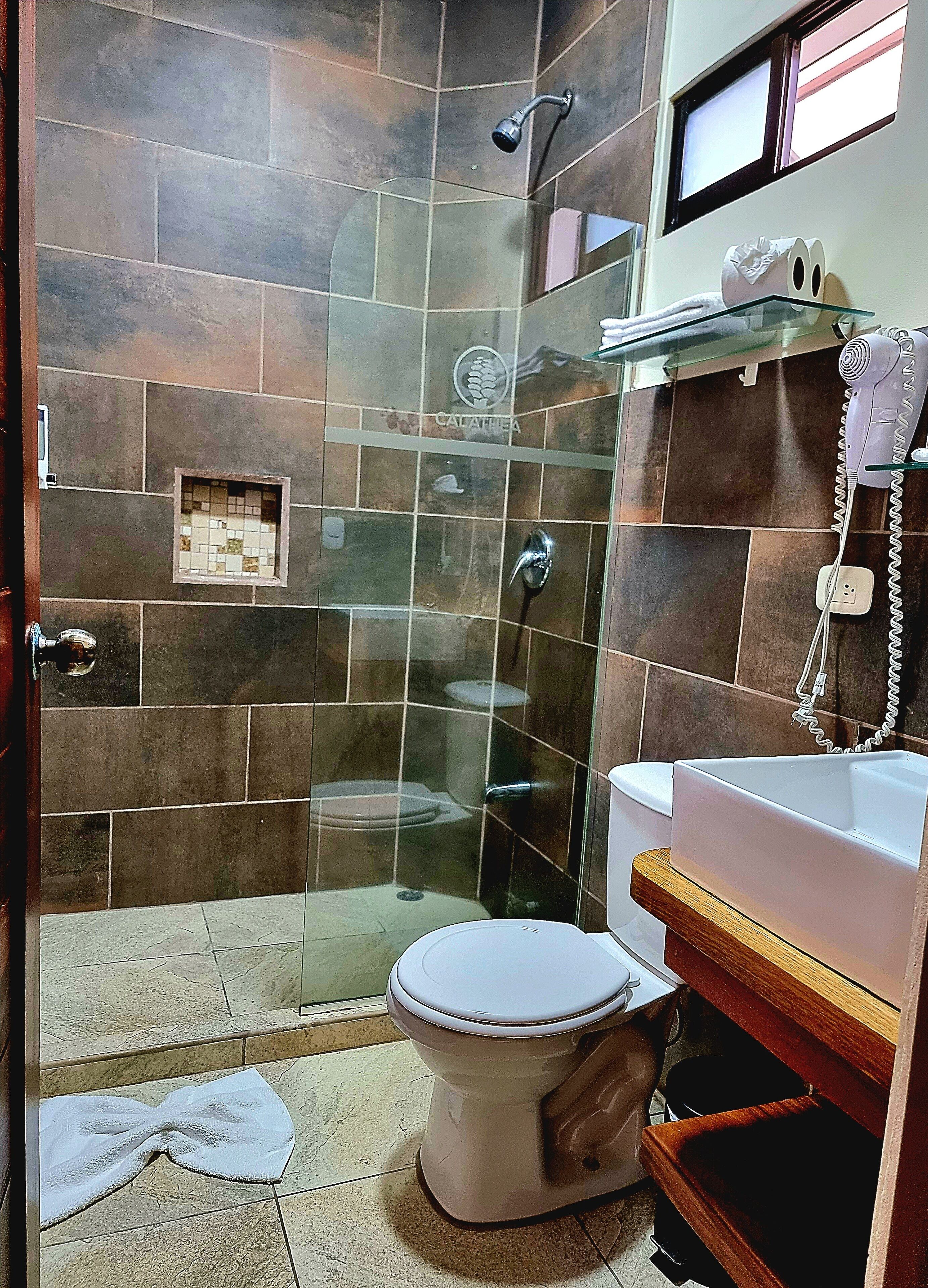 Un baño con ducha compartimentada por vidrio, inodoro y lavamanos con toallero.