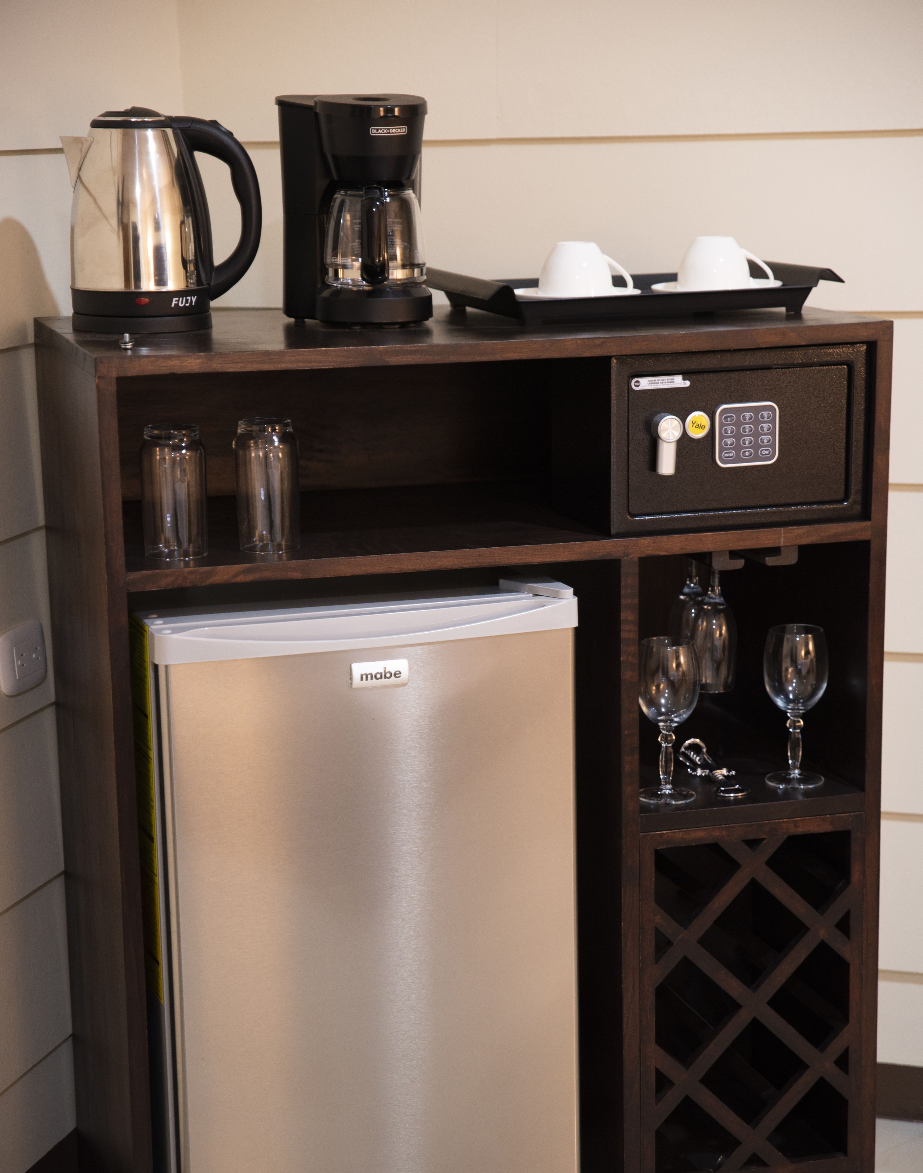 Een minibar met een koffiezetapparaat, twee bekers en een wijnglas.