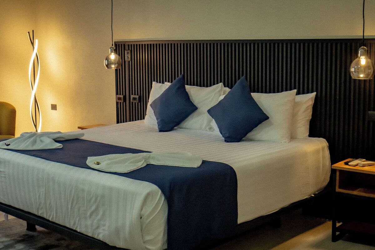 A hotel room with a bed, bedside tables, a chair, and a lamp.