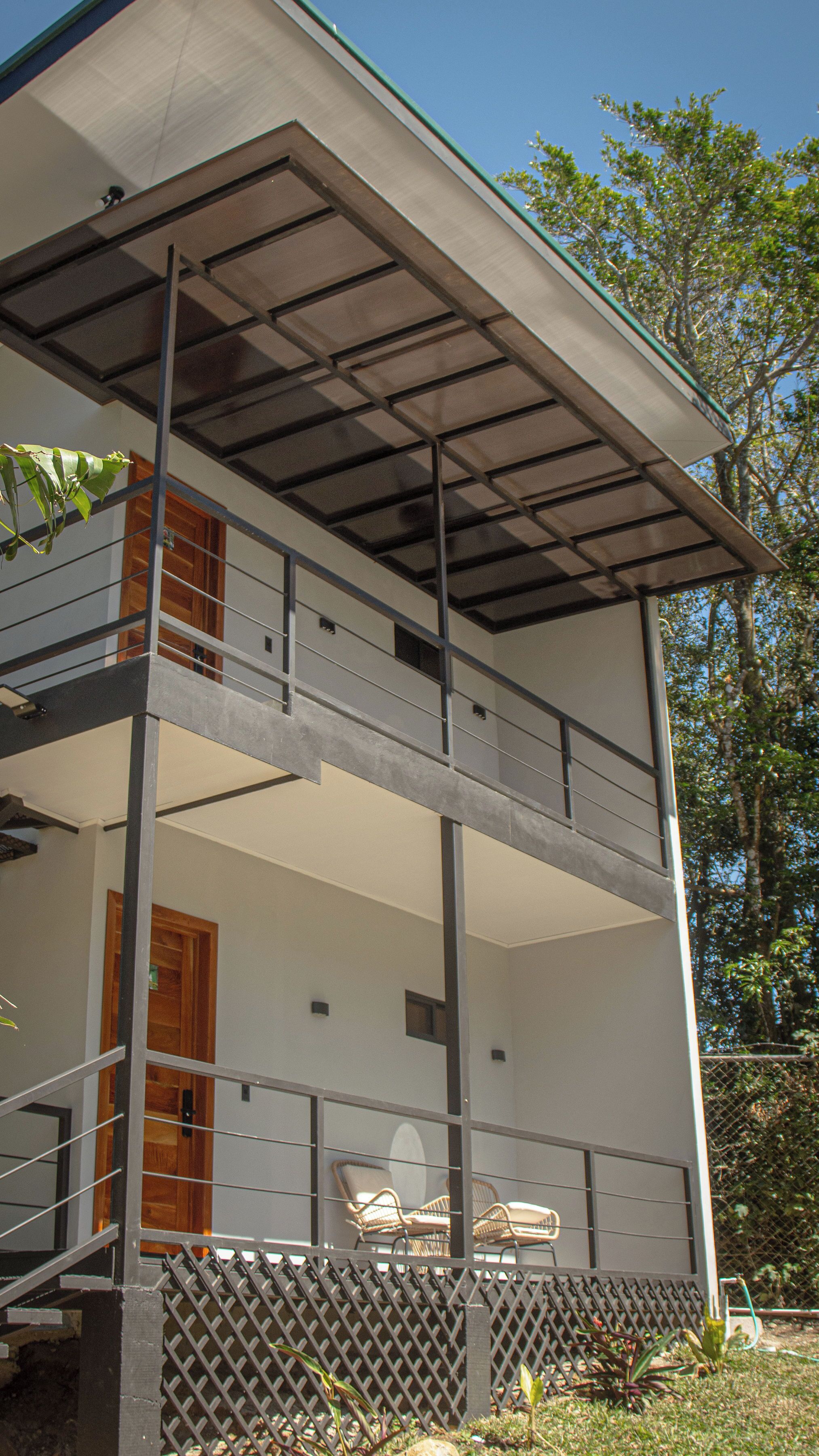 Un edificio de dos pisos con un balcón, una puerta de madera y mesas al aire libre.