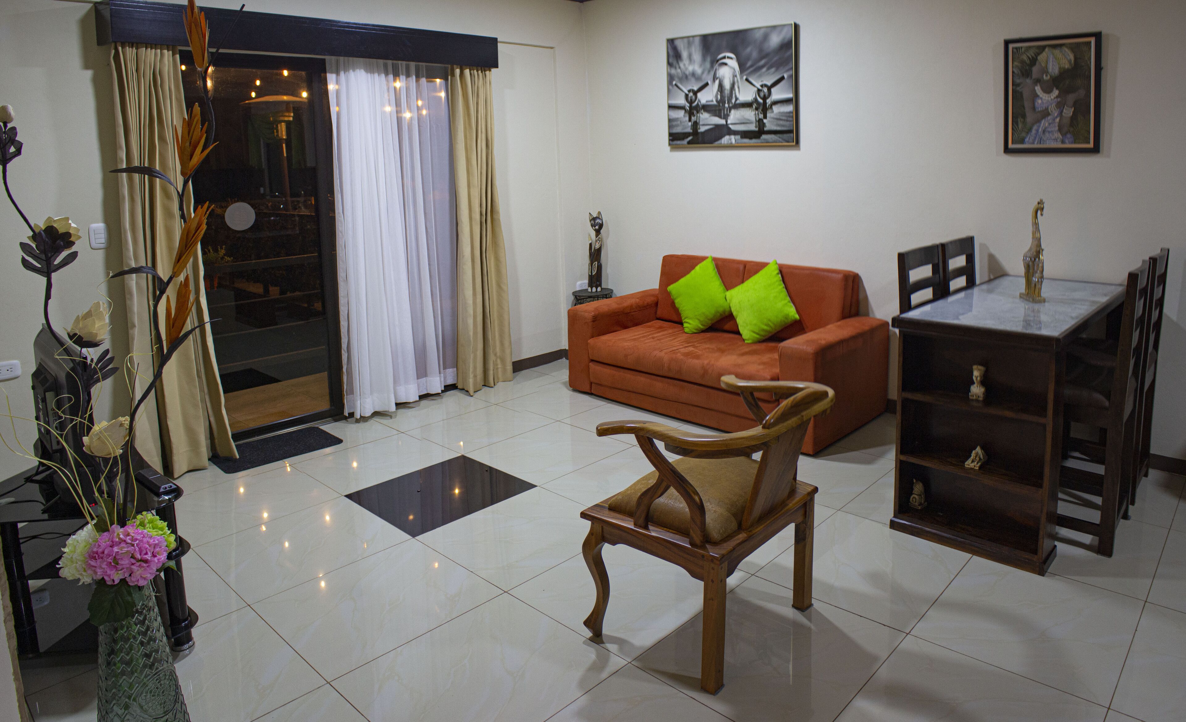 A living room with a sofa, a wooden chair, a dining table, and a vase with flowers.