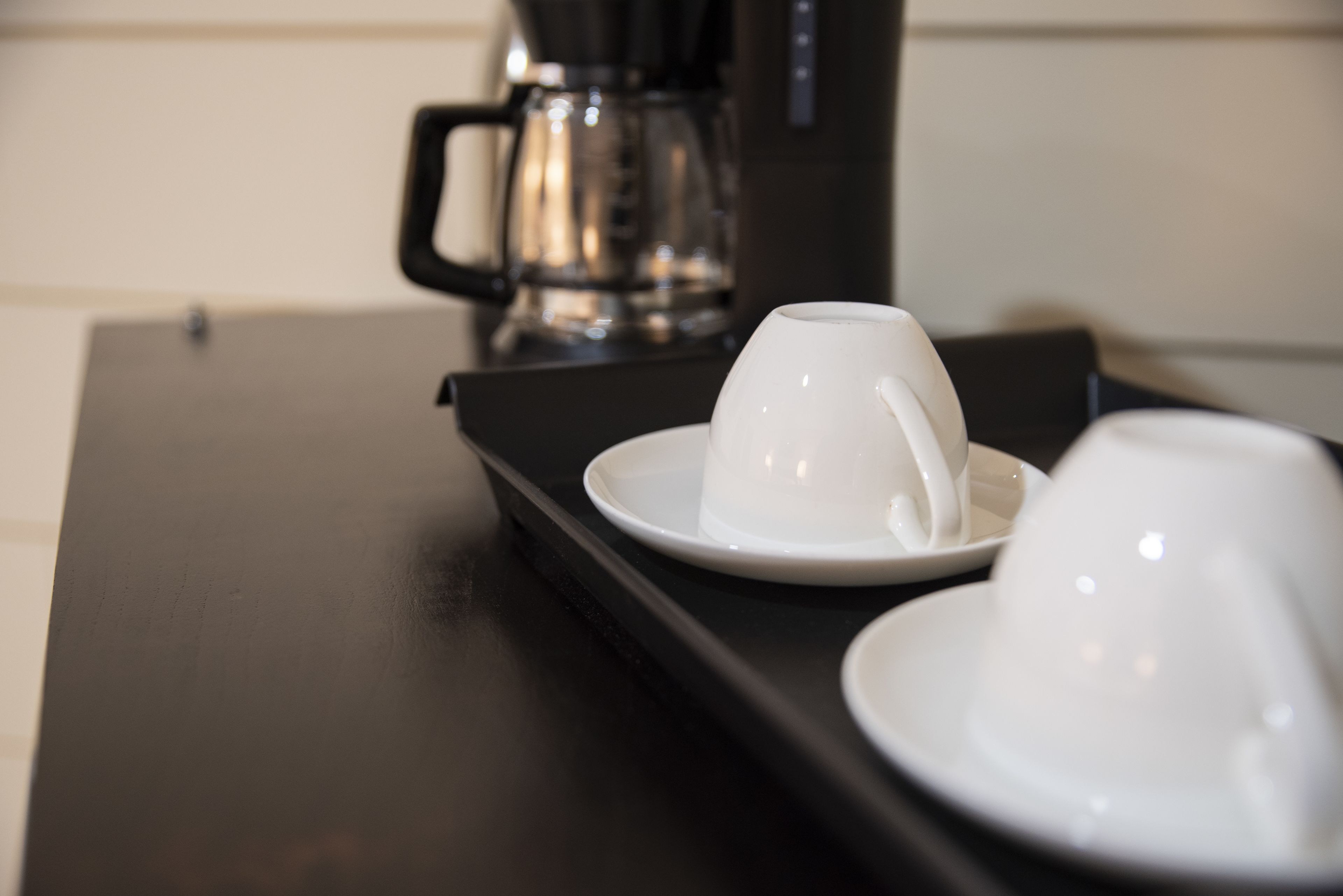 A coffee maker and two white cups on a black tray.