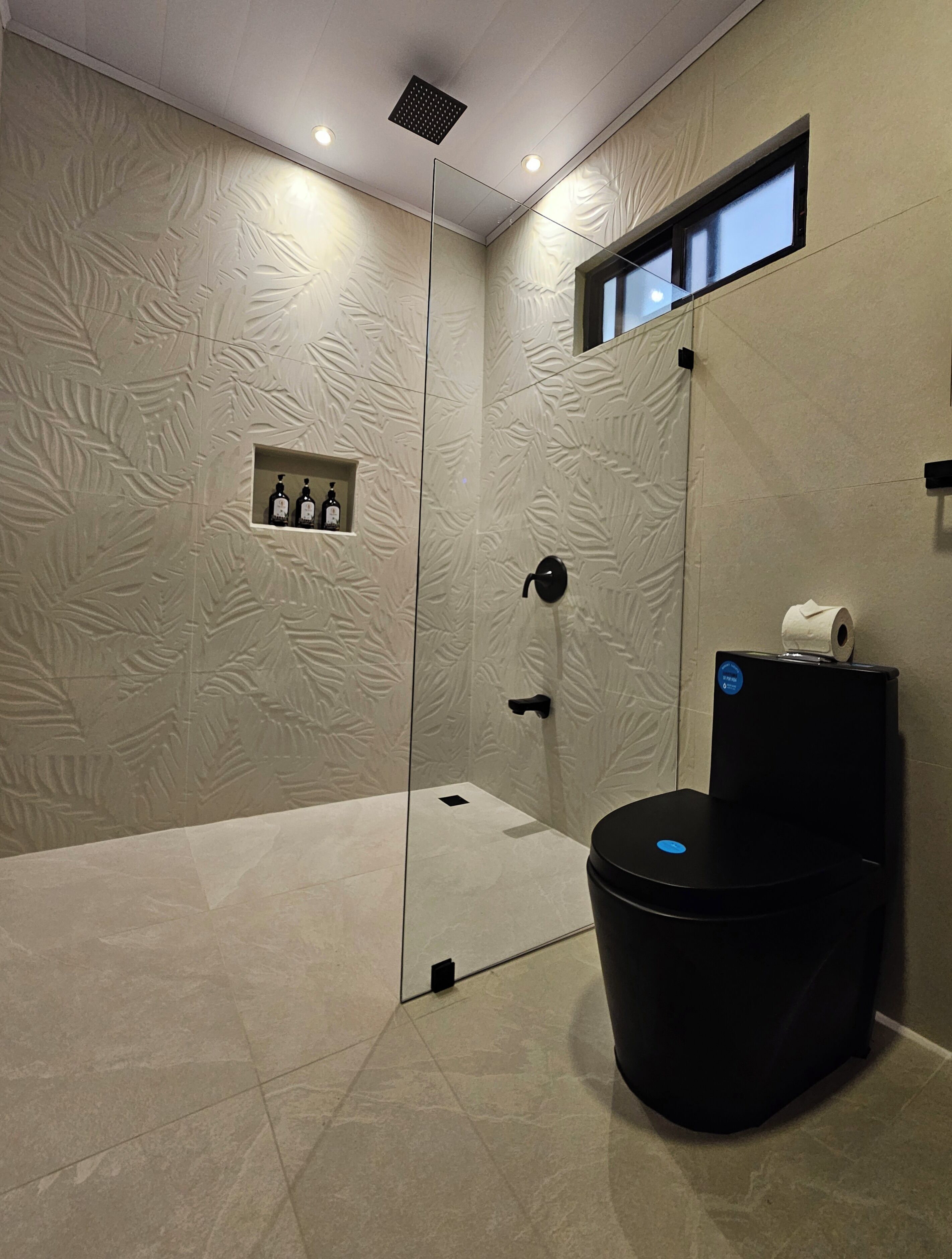 Un baño moderno con cabina de ducha de vidrio, inodoro con panel digital y un pequeño estante con artículos de aseo.