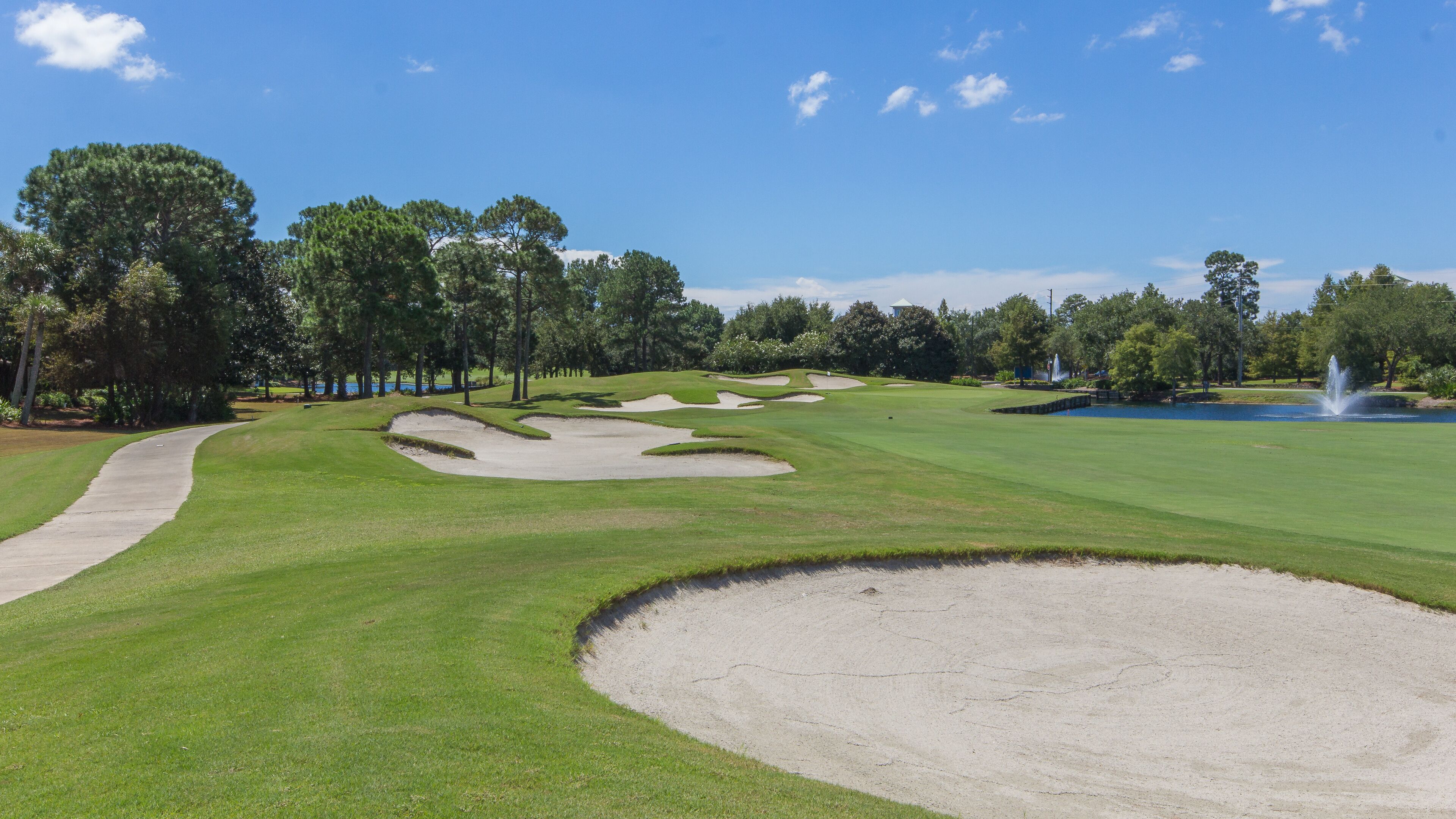 A golf course with sand bunkers, a water feature, and a clear sky.