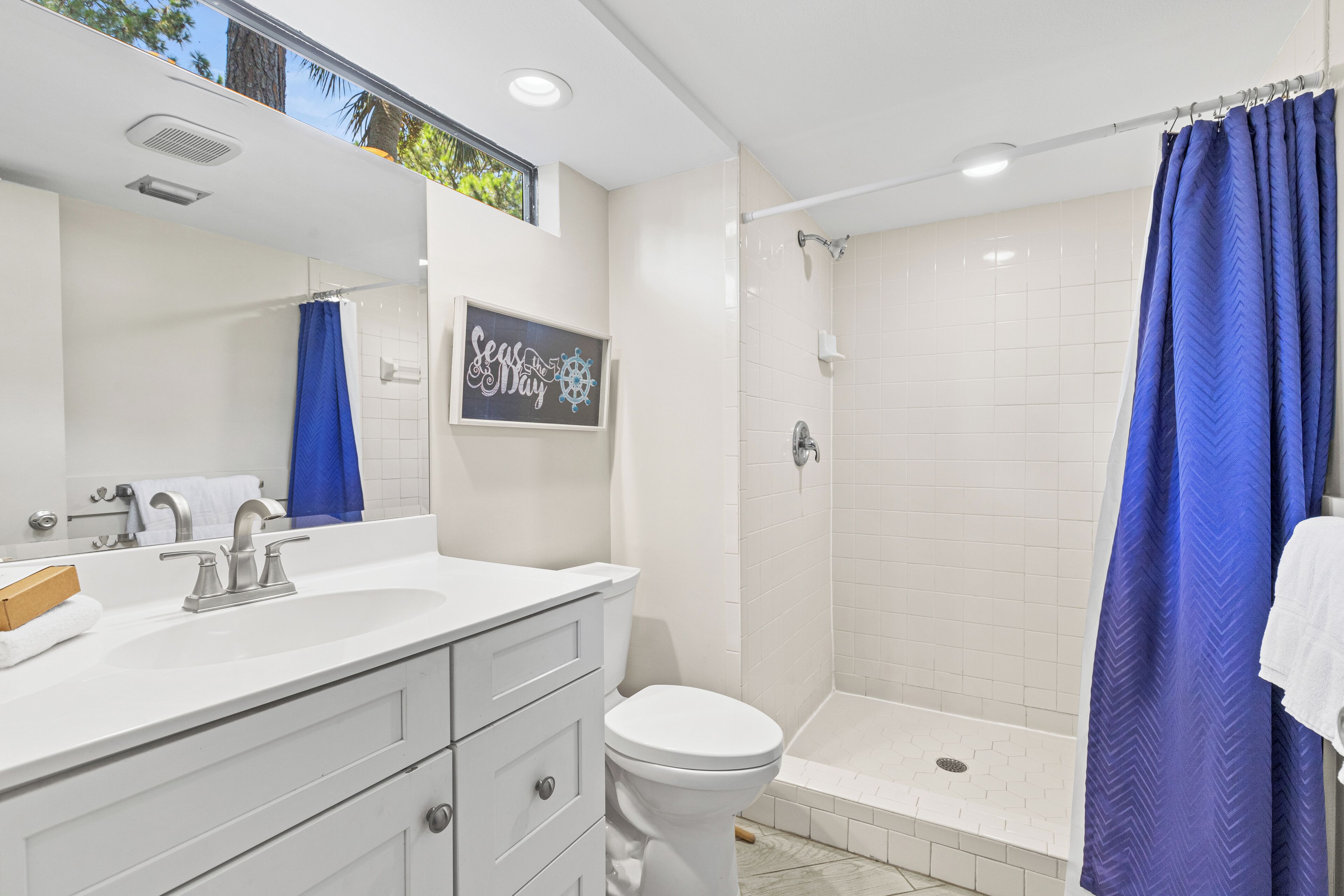 Une salle de bain avec un lavabo blanc, des toilettes, une douche avec un rideau bleu et un panneau indiquant « Séjournez et amusez-vous ».