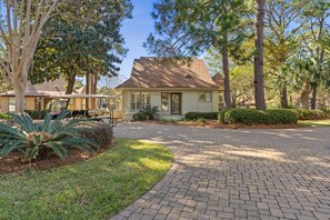 A single-story house with a paved driveway, surrounded by trees and a well-maintained lawn.