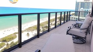 Un balcón con vistas a la playa y al océano. Hay una silla y una mesita.