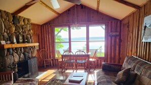 Een gezellig vakantiehuisje met een stenen muur, houten meubels en een groot raam met uitzicht op een waterpartij.