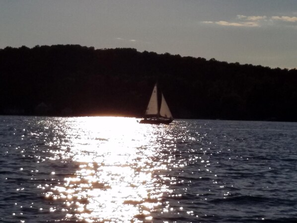 Un velero en aguas tranquilas, con una costa boscosa al fondo.