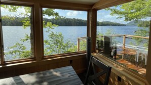 A cabin with a wooden interior, large windows overlooking a lake, and a deck area with outdoor furniture.