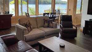 A cozy living room with a large window overlooking a lake, a leather sofa, a wooden coffee table, and a leather armchair.