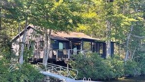 A cabin with a dock extending into a body of water, surrounded by dense foliage.