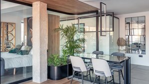 A modern living room with a glass partition, a large potted plant, and a dining area with a glass table and chairs. - ChezmoiHomes Luxury Alhambra Penthouse Collection Alhambra (Granada)