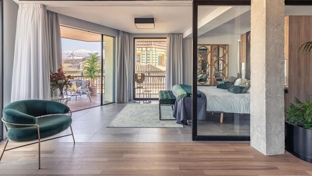 A modern bedroom with a large sliding glass door leading to a balcony, a green chair, and a bed with a view of a traditional building. - ChezmoiHomes Luxury Alhambra Penthouse Collection Alhambra (Granada)