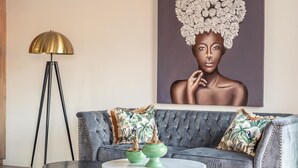 A modern living room with a tufted grey sofa, two green decorative vases, a gold floor lamp, and a large abstract painting on the wall. - ChezmoiHomes Luxury Alhambra Penthouse Collection Alhambra (Granada)