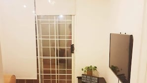 A small living room with a sofa, a TV mounted on the wall, a sliding glass door, and a small table with a plant. - Vista Hermosa -libre de humo- (Ensenada)
