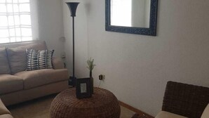 A living room with a sofa, a round wicker ottoman, a floor lamp, and a mirror on the wall. - Vista Hermosa -libre de humo- (Ensenada)