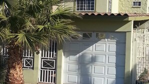 A two-story house with a red-tiled roof, a white garage door, and a palm tree in the foreground. - Vista Hermosa -libre de humo- (Ensenada)