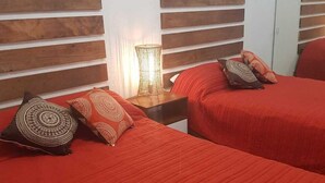 A room with two beds, each with red bedding and patterned pillows. There is a nightstand with a lamp between the beds. - Vista Hermosa -libre de humo- (Ensenada)