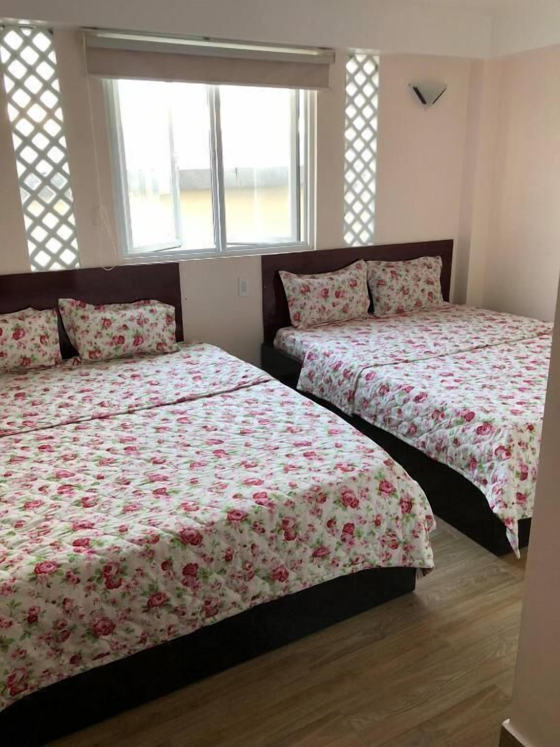 Two beds with floral bedding, a window with a view, and a wall-mounted light fixture.