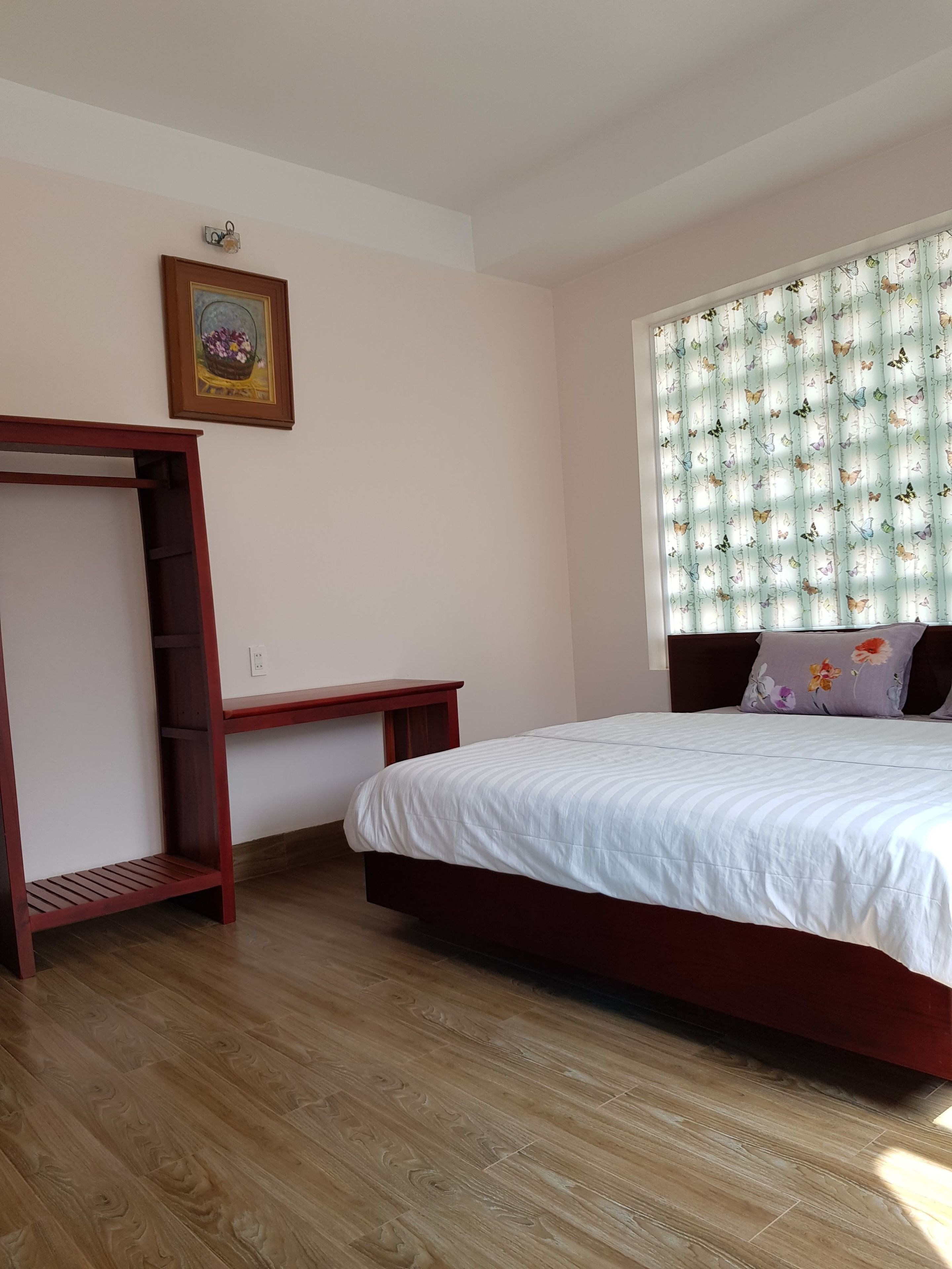 Un dormitorio con una cama de madera, una mesita de noche, un armario y una ventana con cortinas de mariposas.